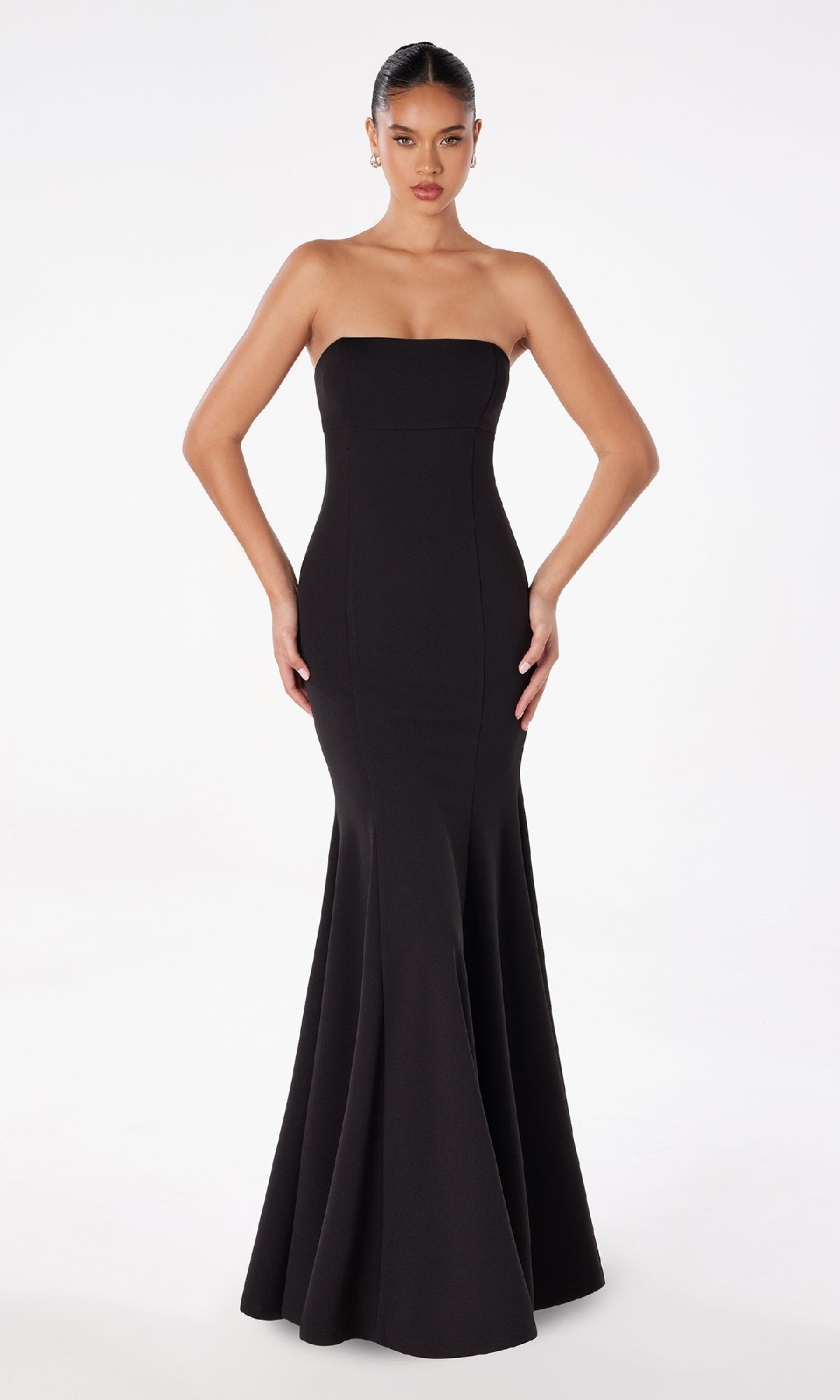 A woman stands against a white background wearing the Lace-Up Strapless Long Prom Dress: Astee T2010—an elegant, form-fitting black evening gown with a flared hem.